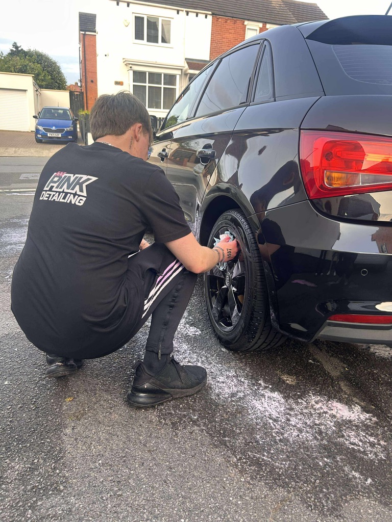 Detailer cleaning wheel on a black SUV